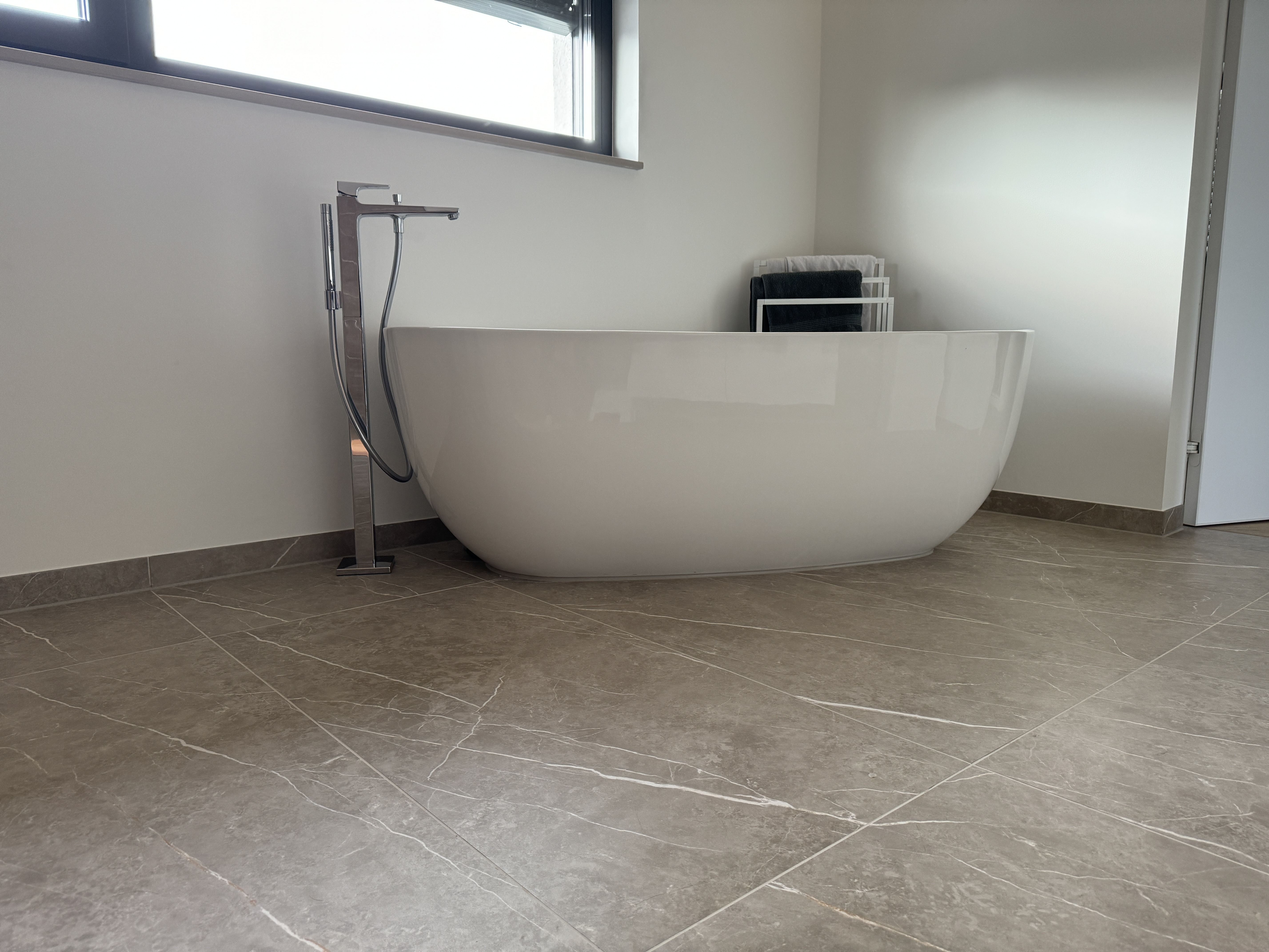 Weiße freistehende Badewanne auf Bodenfliesen in Natursteinoptik