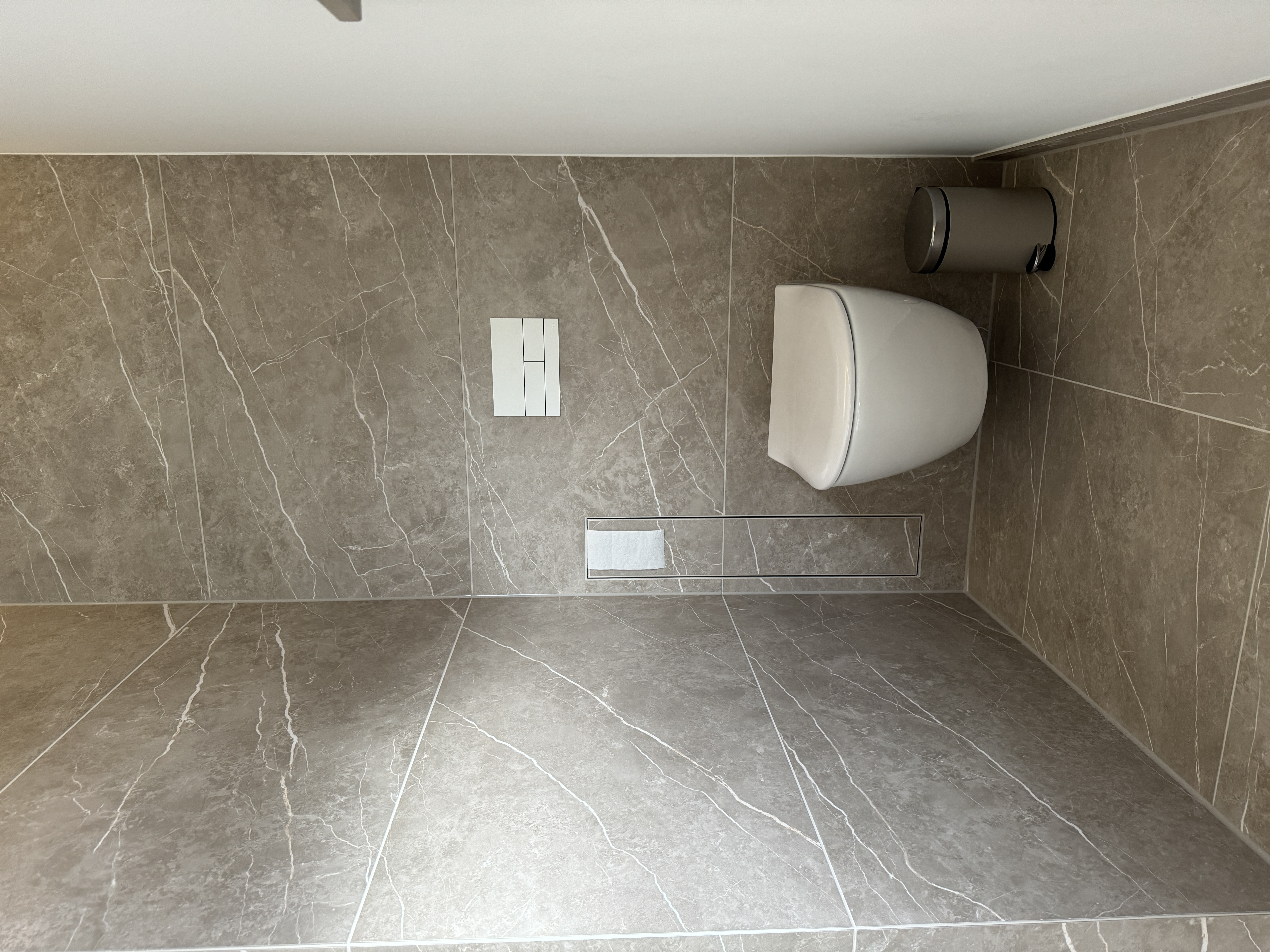 Wandhängendes WC in einem mit Natursteinoptik gefliesten Bereich