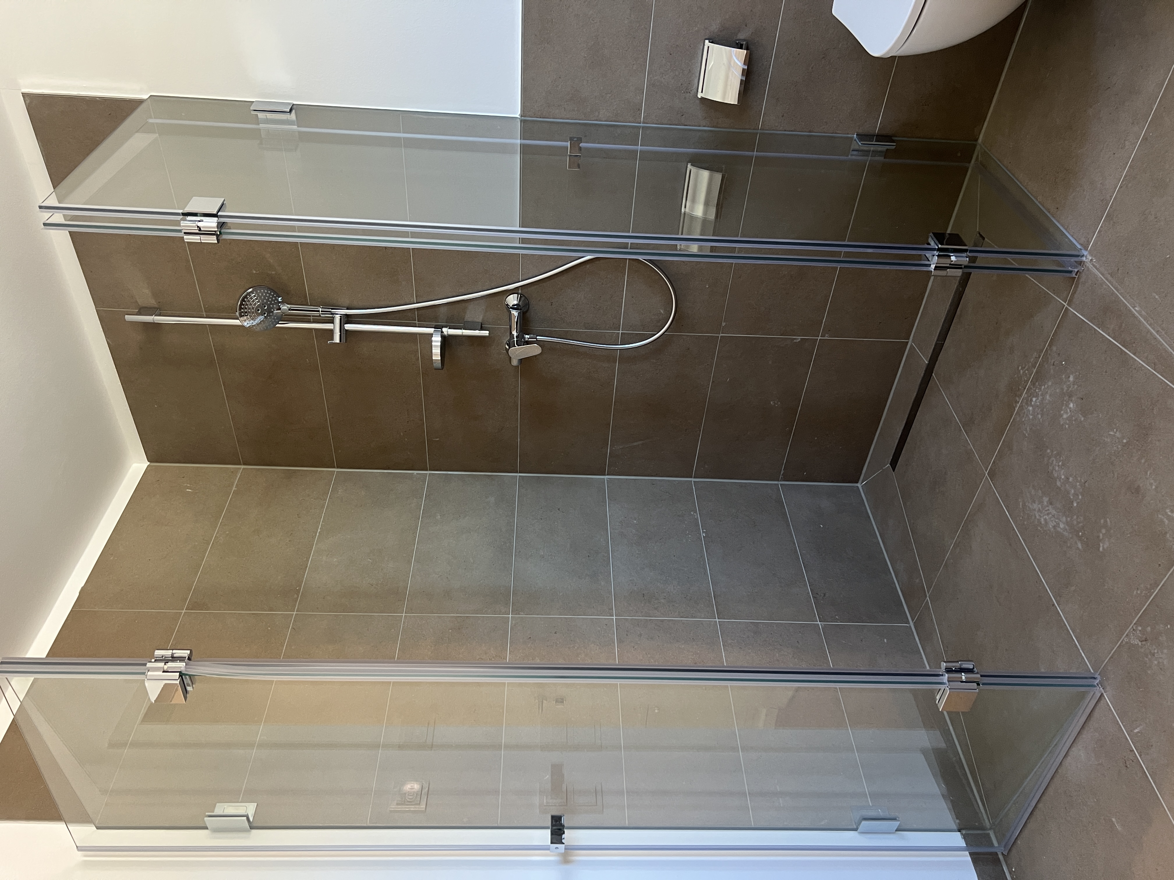 Glasabtrennung der bodenebenen Dusche vor braunen Wandfliesen