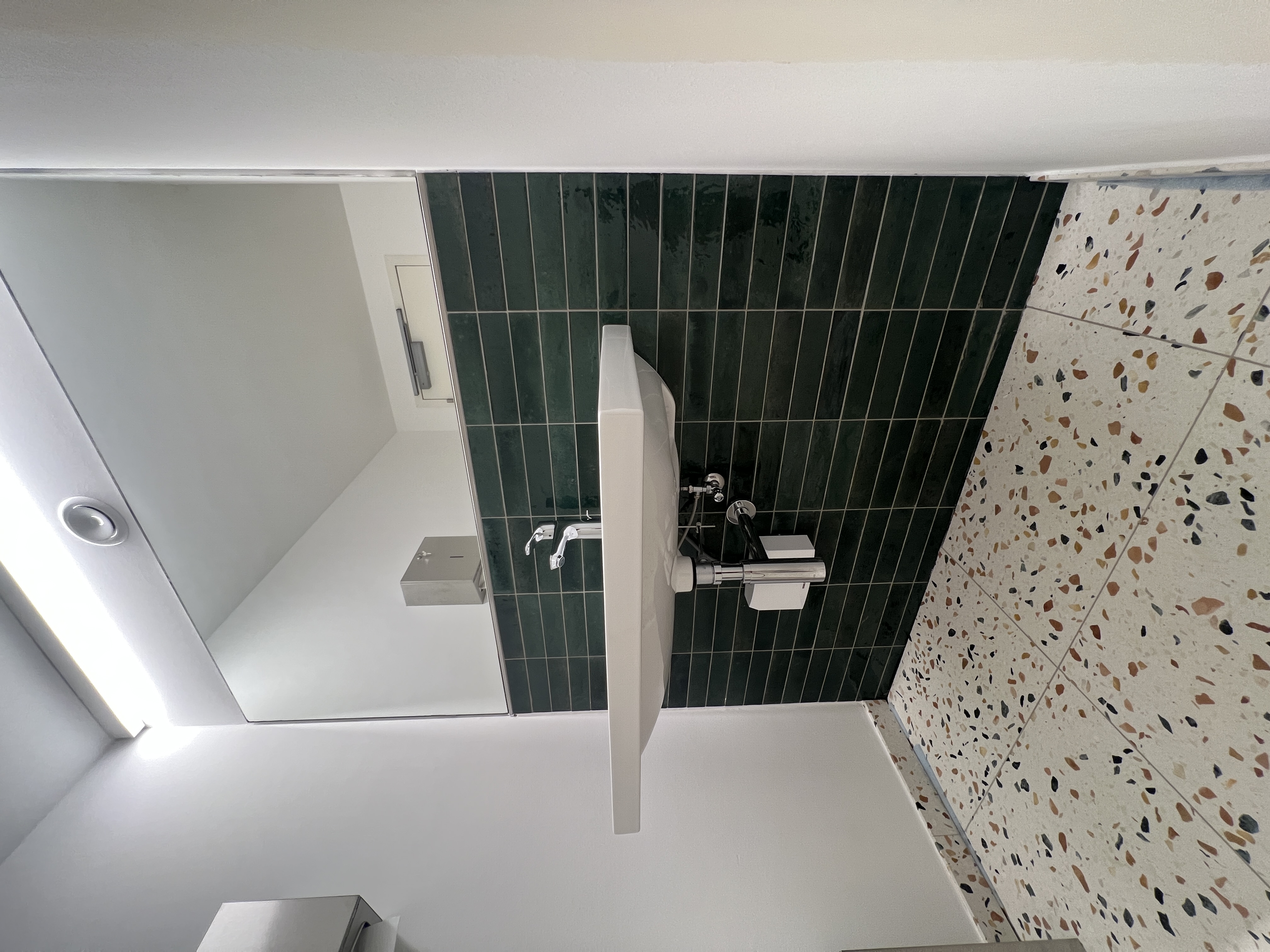 Waschtisch im Sanitärbereich der Gewerbeeinheit mit grünen Fliesen und Terrazzo-Optik