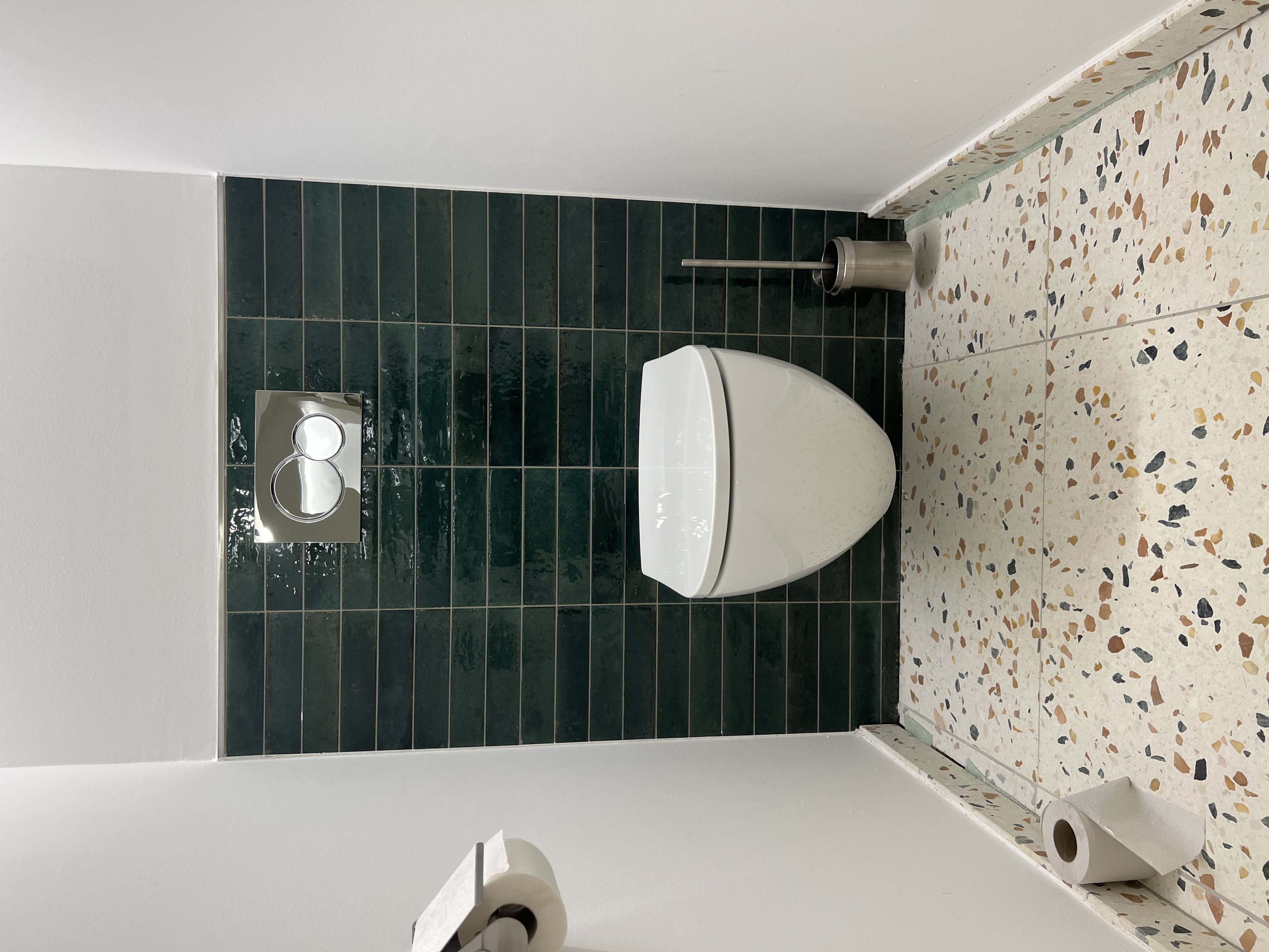 WC der Gewerbeeinheit mit grünen Kleinformatfliesen und Terrazzo-Optik