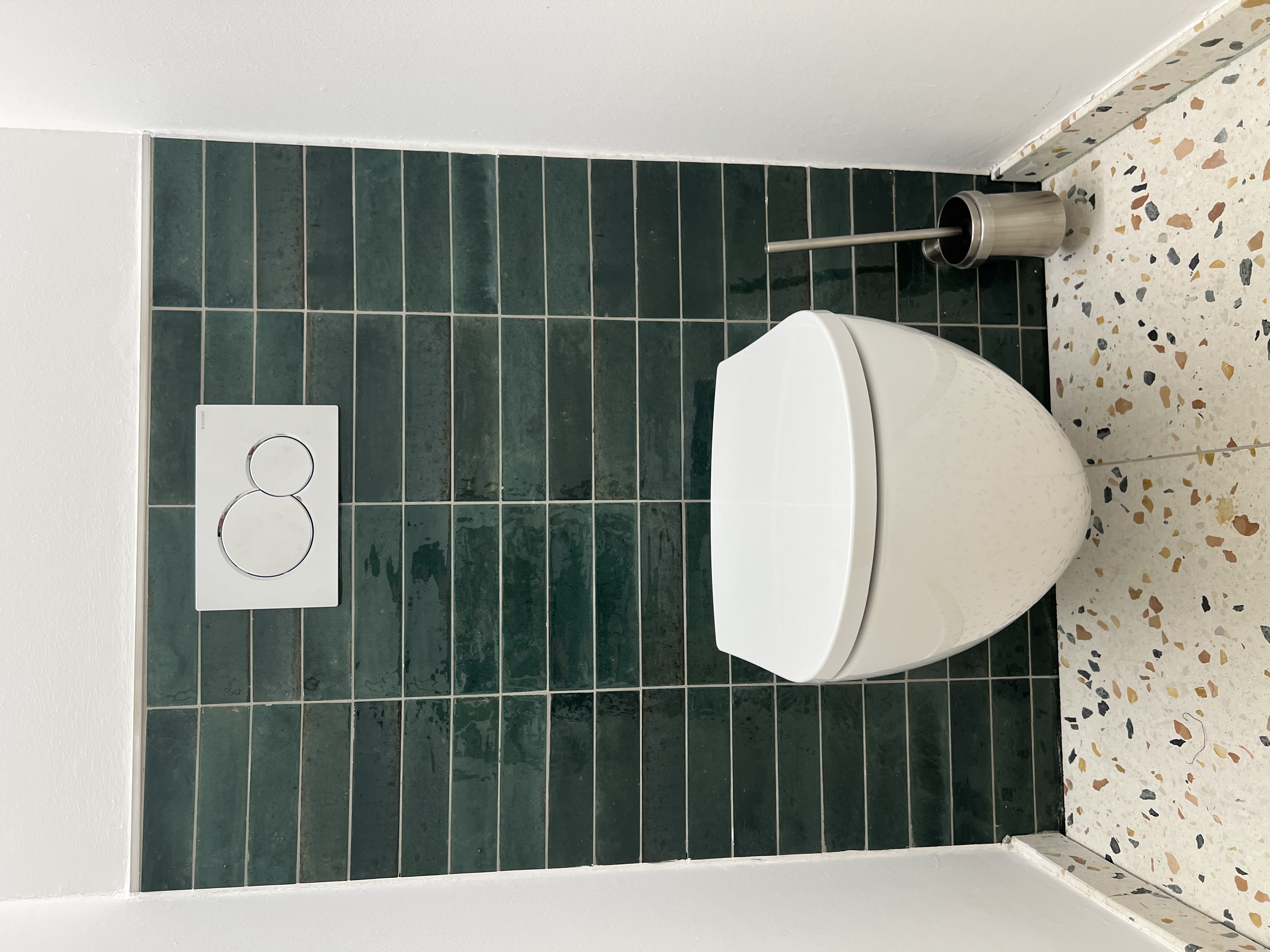WC mit grün gefliester Vorwand und Betonwerksteinboden in Terrazzo-Optik